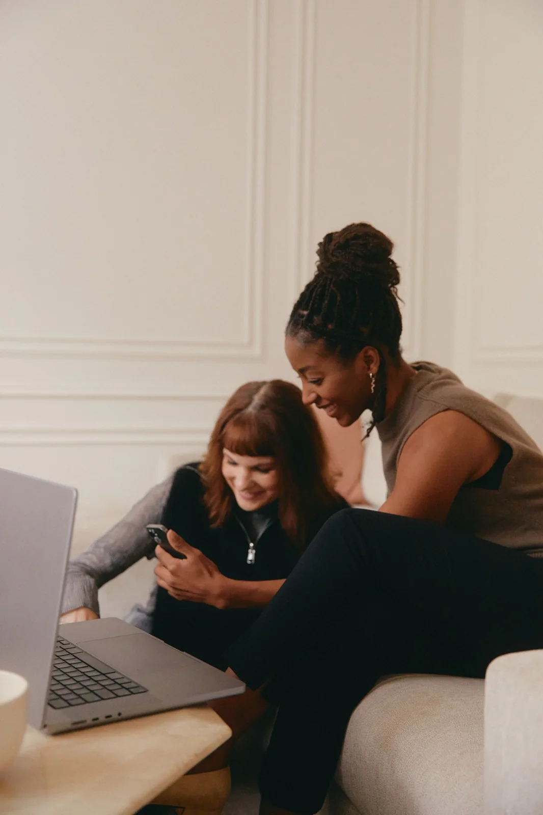 Two people reviewing information on a phone beside a laptop